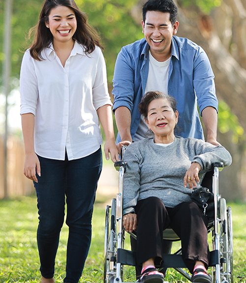 Smiling family walking in a park with their grandmother in a wheelchair